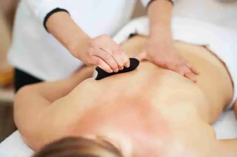 Gua Sha Treatment, a gua sha tool being used on the back of a massage client