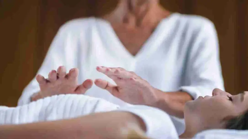 Reiki Energy Healing Being preformed on a woman on a massage table, hands gently positioned over her body.